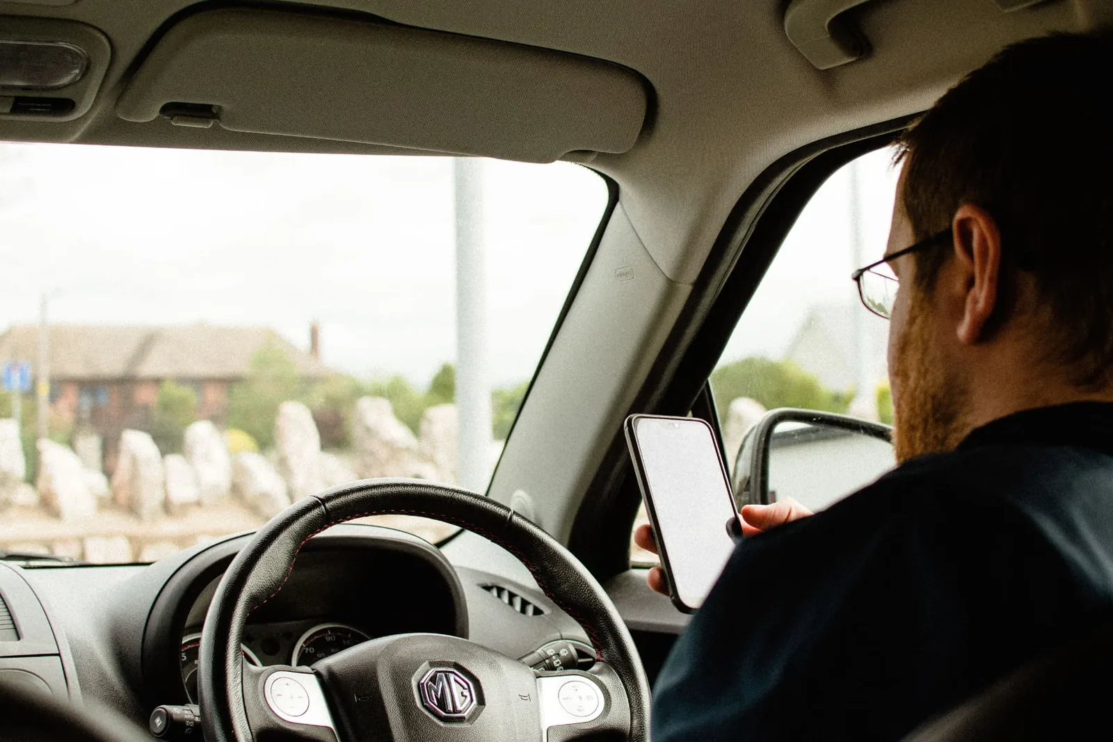 Außendienstmitarbeiter im Auto, der am Steuer auf sein Smartphone schaut